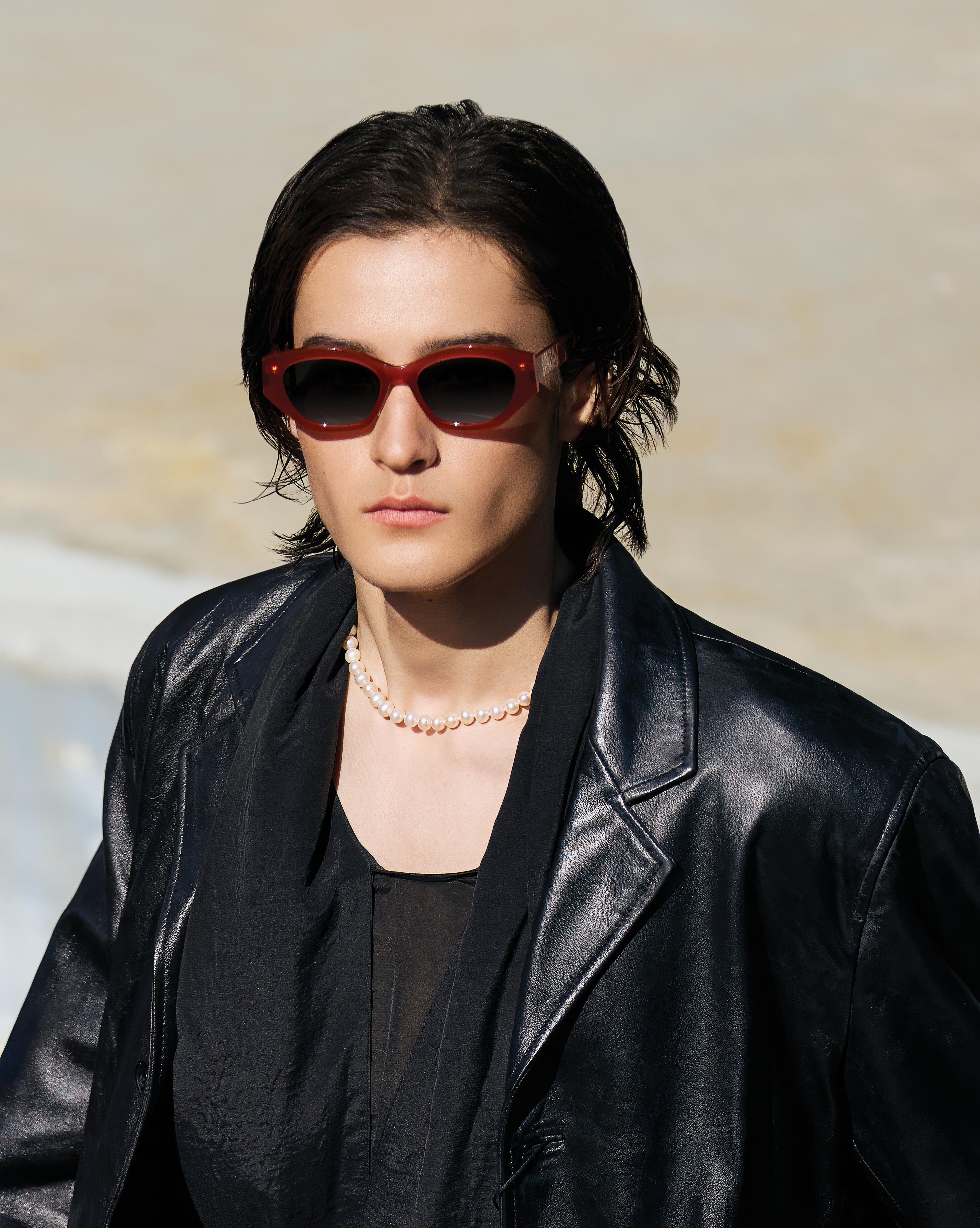 Person wearing red sunglasses and a black leather jacket against a neutral background