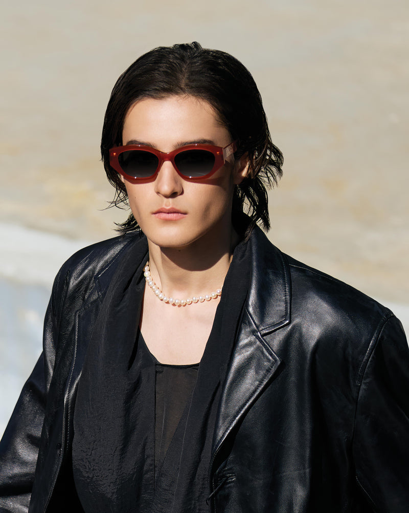 Person wearing red sunglasses and a black leather jacket against a neutral background