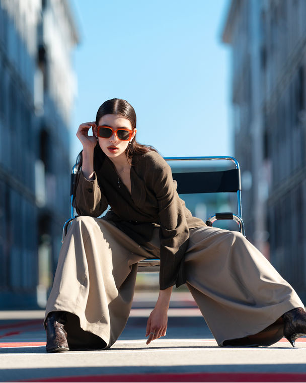 Woman in sunglasses and a coat sitting on a chair in an urban setting